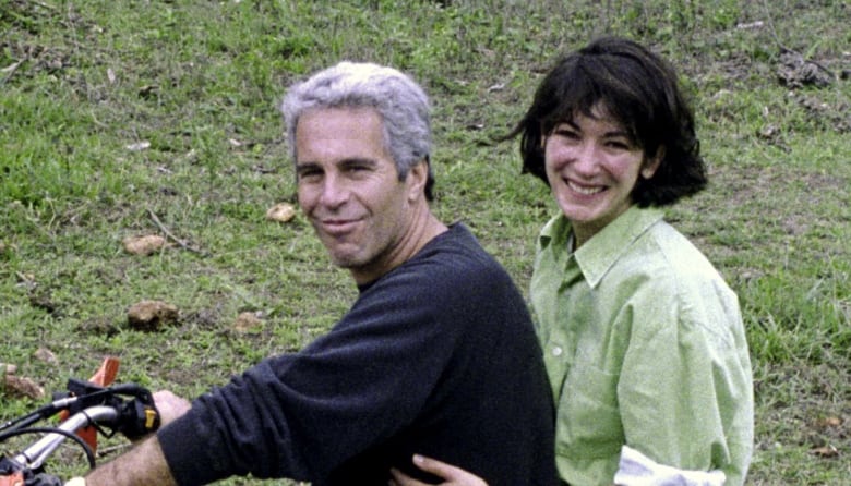 A man with grey hair holds the handlebars of a bike while a woman with black hair sits on the back of the bike with her arms around his waist.