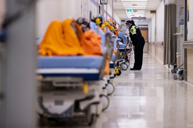 A hospital hallway is crowded with patients lying on stretchers as a paramedic checks on one of them.