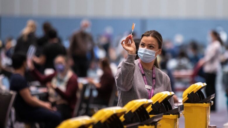 A female medical worker wearing a mask holds up a dose of COVID-19 vaccine at a Vancouver immunization clinic in January 2022. 