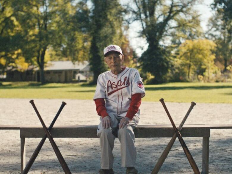 A man sits on a bench wearing a baseball uniform