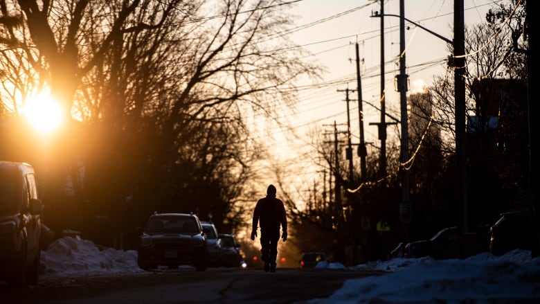 Someone's silhouetted against the setting sun as they walk down a street in winter.