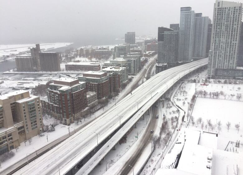 A snowy highway snakes through a dense collection of buildings.