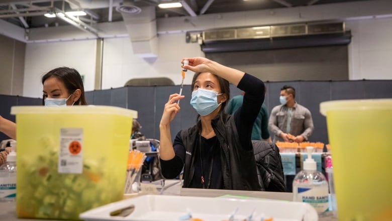 A COVID-19 vaccination clinic at the Vancouver Convention Centre in Vancouver, British Columbia on Thursday, Jan .13, 2022. See female medical personnel holding syringe.