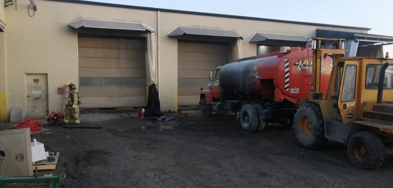 A firefighter and a tanker truck in front of bay doors.