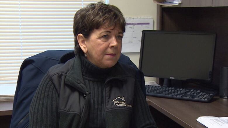 Woman with short dark hair sits at a computer desk.