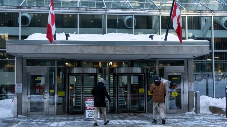 A building with two Canadian flags, and people walking in.