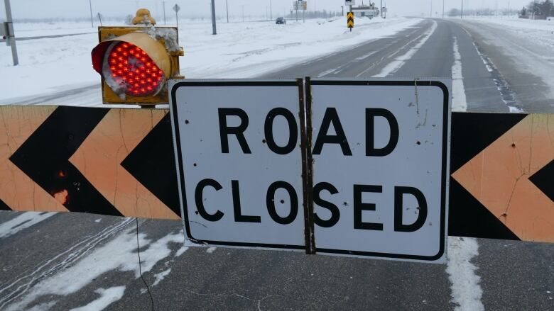 A sign across a snowy highway says Road Closed