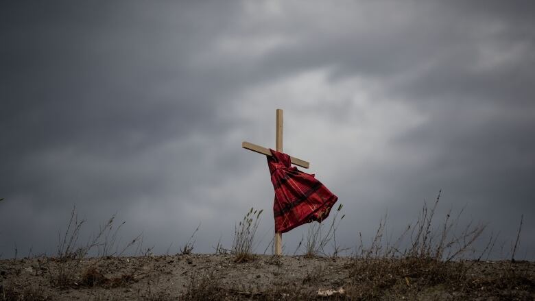 A red dress hangs from a cross on a patch of ground.