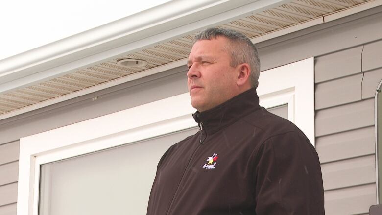 Man with serious expression on face wearing a black, lightweight jacket stands outside building.