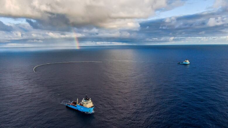 Two ships about a kilometre apart deploy between them on the ocean on a sunny day with a cloud-filled sky.