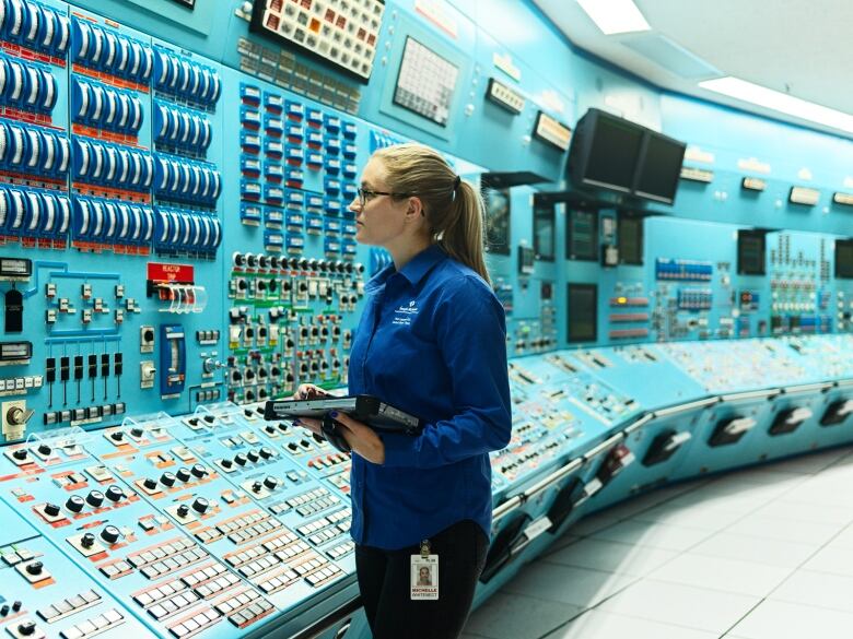 A woman standing in a teal blue control room