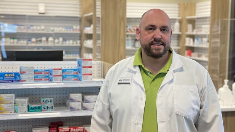 A portrait of a man wearing a white lab coat in a pharmacy.