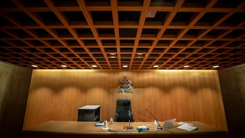 A courtroom interior with a crest of British Columbia behind a judge's desk.