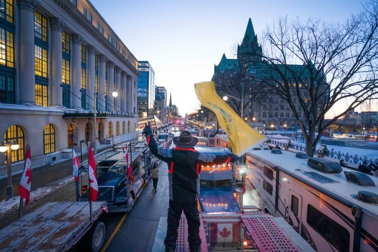 Someone in a cowboy hat waves a yellow flag over rows of trucks parked on a city street.