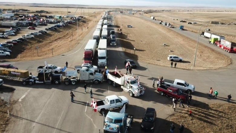 A long line of semi trucks lineup down a highway.