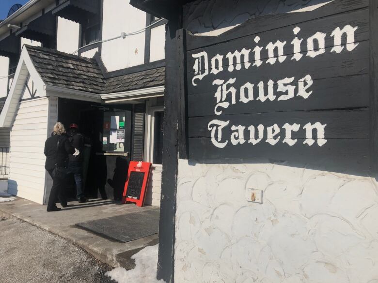 People enter a pub with a sign that says Dominion House Tavern on it.