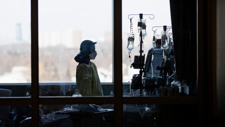 A nurse looks at IV bags and monitors while attending to a patient in the ICU. There is a large window in the background.