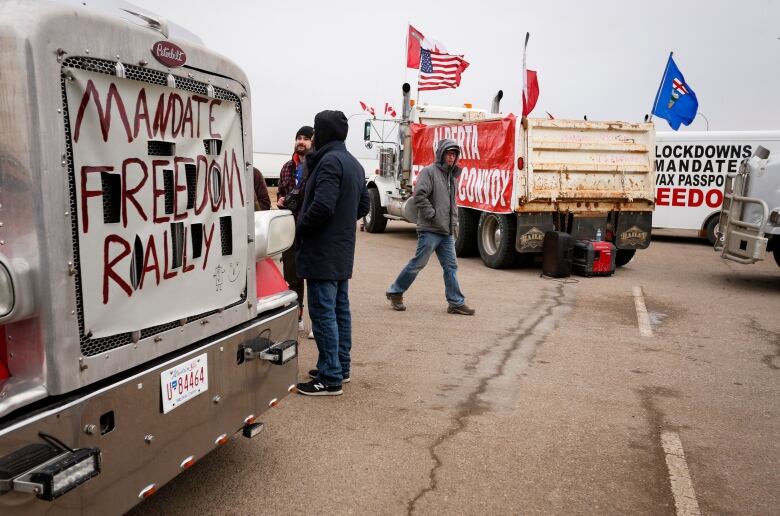 Convoy protesters walk among trucks emblazoned with protest signs.