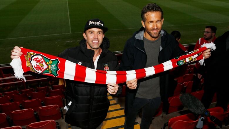 Two men hold a soccer team's branded scarf.