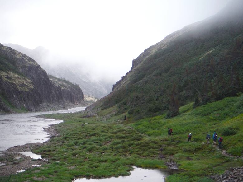 Hikers are seen walking beside a river through the mountains.