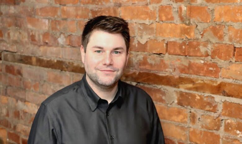 A man poses in front of a brick wall