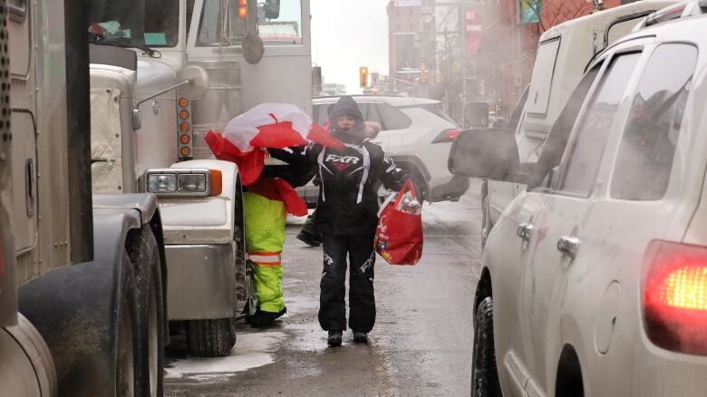 A person standing between idling trucks and cars waves a Canadian flag