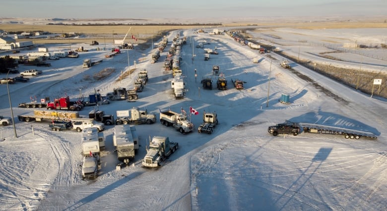 A look from above at tractor-trailers and other large vehicles parked on a snowy prairie highway.