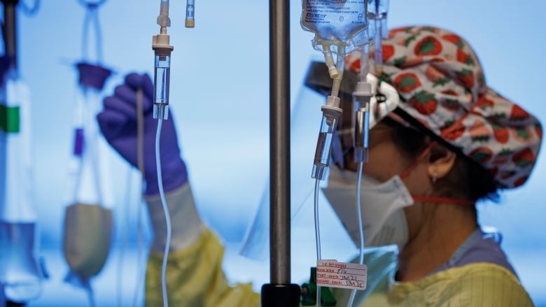 A nurse, in a yellow gown and red and white cap, adjusts IV cords