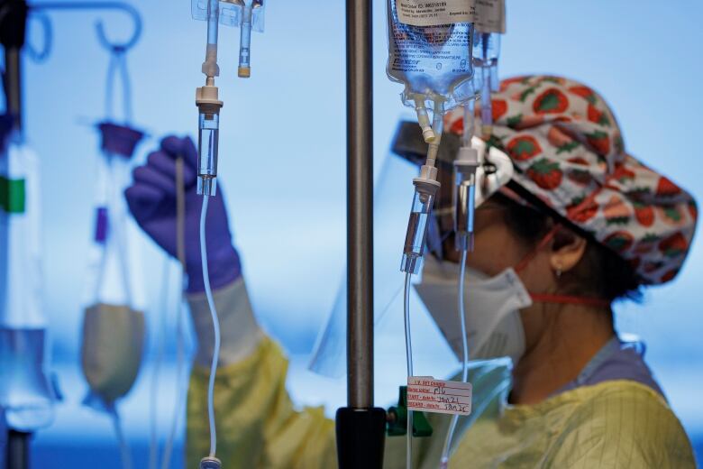 A nurse, in a yellow gown and red and white cap, adjusts IV cords