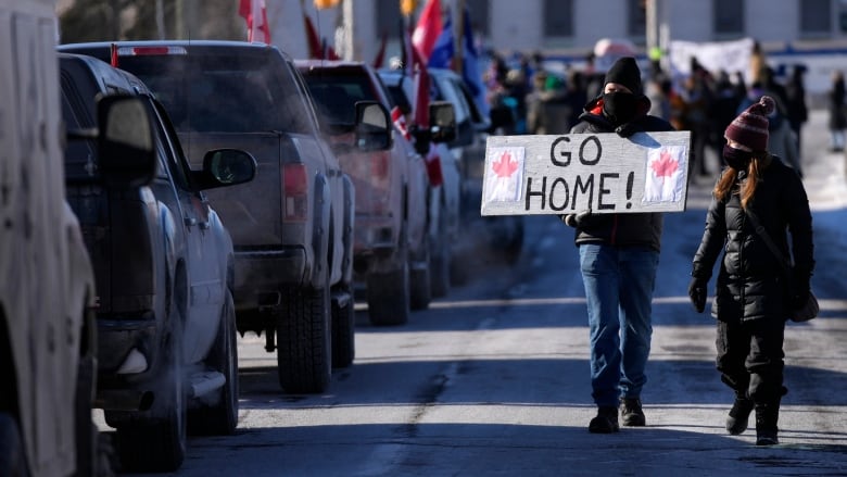 A resident holds a sign towards protesters as they participate in a counter protest to stop vehicles from driving in a convoy en route to Parliament Hill, on the 17th day of a protest against COVID-19 measures that has grown into a broader anti-government protest, in Ottawa, Sunday, Feb. 13, 2022. THE CANADIAN PRESS/Justin Tang