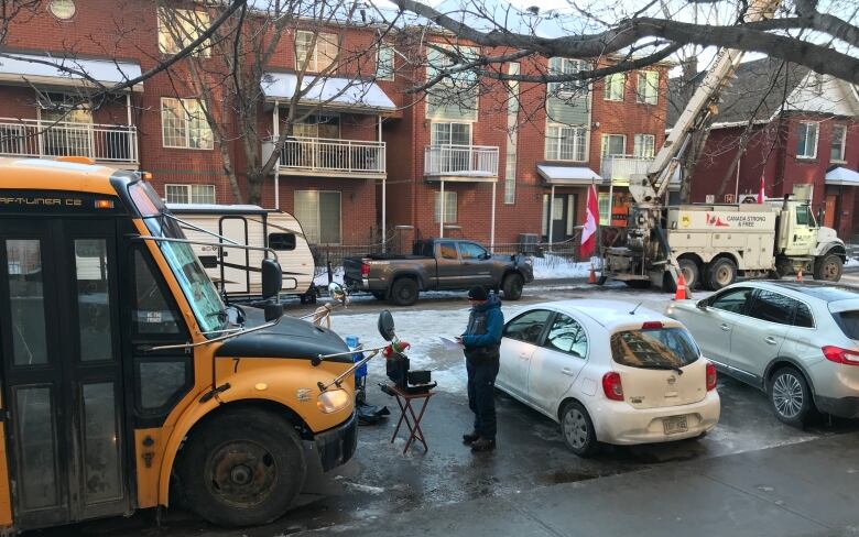 Vehicles, some of them large and many with Canada flags, are parked on a city's residential street in winter.