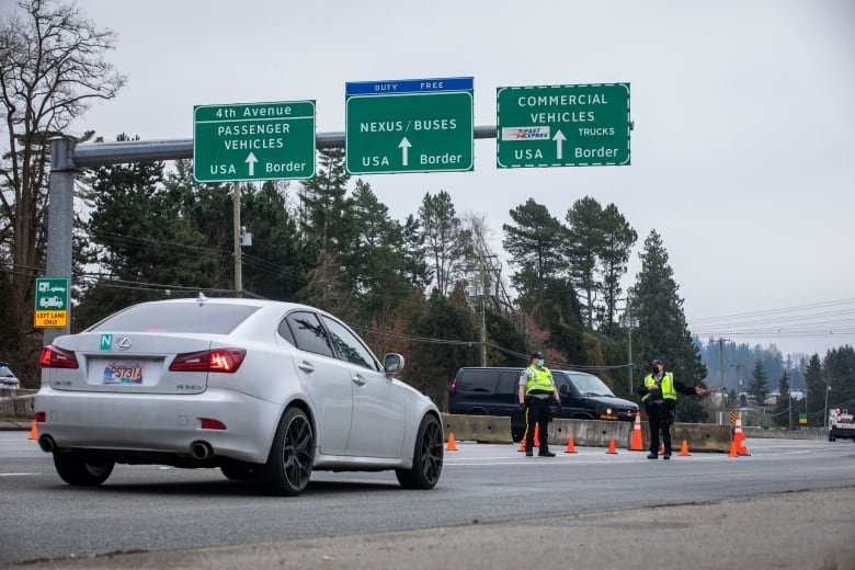 A car approaches a police checkpoint below green signs.