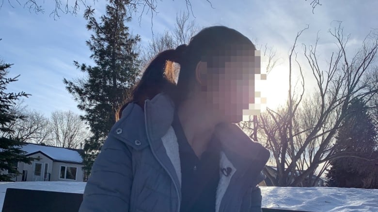 Woman with ponytail sits on bench in the sunshine. Her face is blurred out for security reasons.