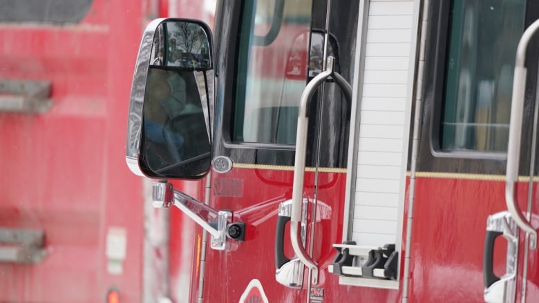 Close up of a bright red fire truck, showing the side mirror and driver door.