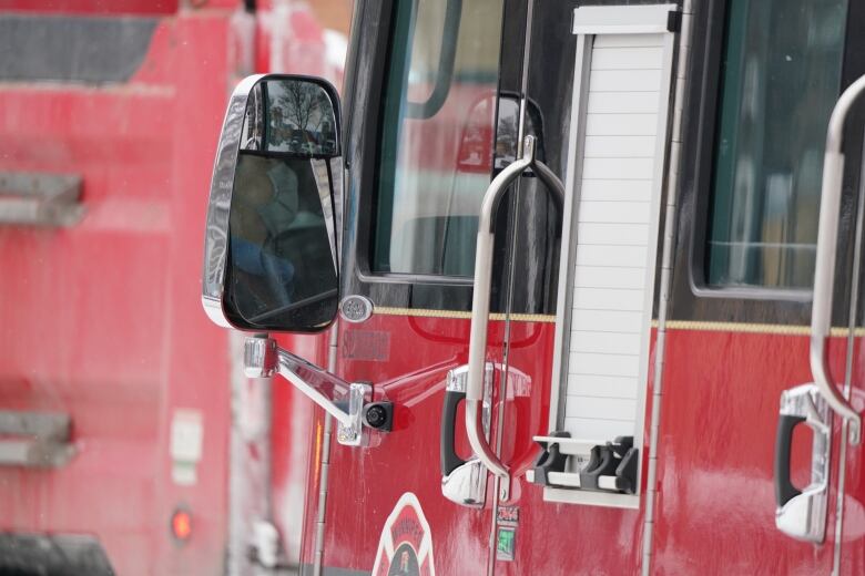 Close up of a bright red fire truck, showing the side mirror and driver door.