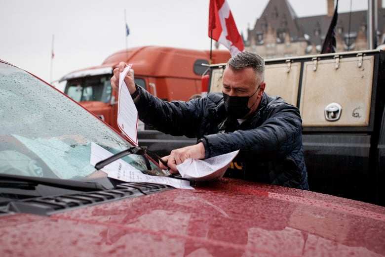 A police officer leaves a notice on the windshield of a vehicle.