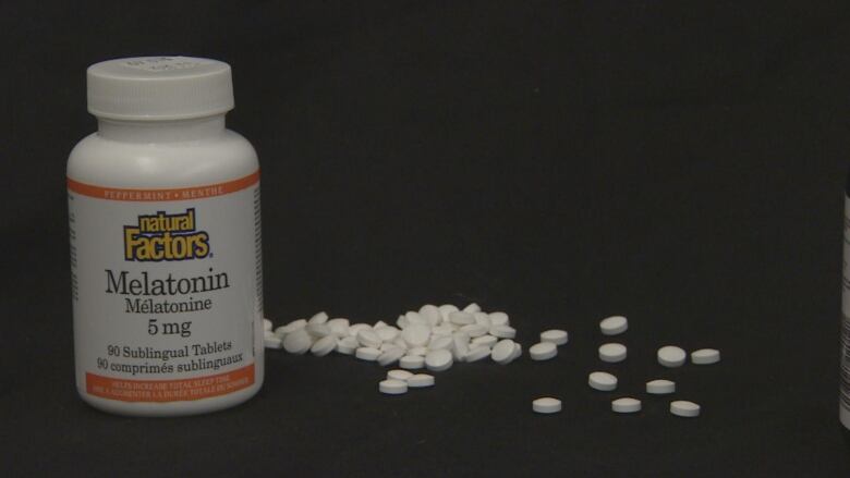 A container of melatonin pills stands beside several spilled drops.