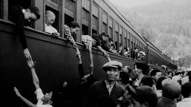 Old archival photo of passengers in a crowded train and onlookers on a platform. 