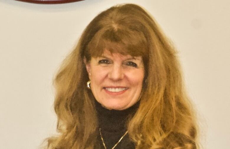 A smiling woman stands in front of a plain background, wearing a mayoral Chain of Office around her neck. 