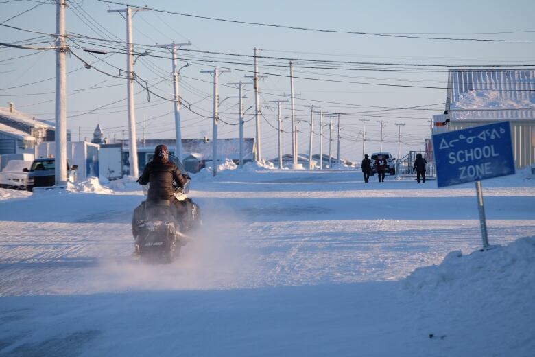 A snowmobiler drives down a snowy street.