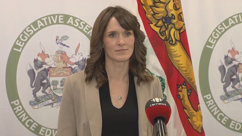 Woman with long brown hair, dressed in black shirt and taupe blazer, speaks into a CBC microphone. 