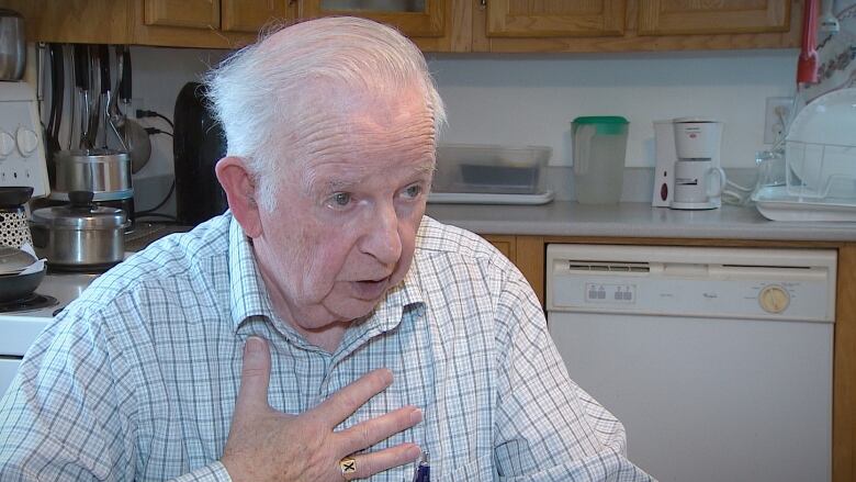 A man with white hair gestures as he talks in his kitchen.