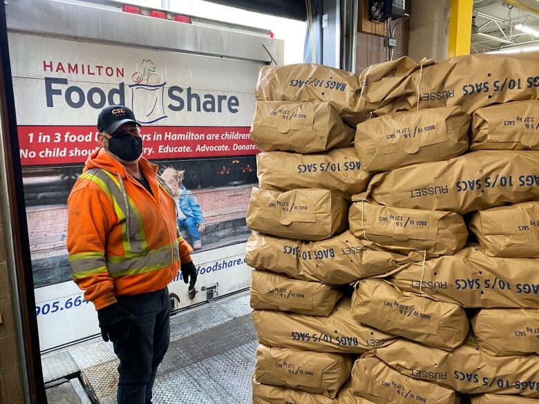 man stands by stack of potato bags