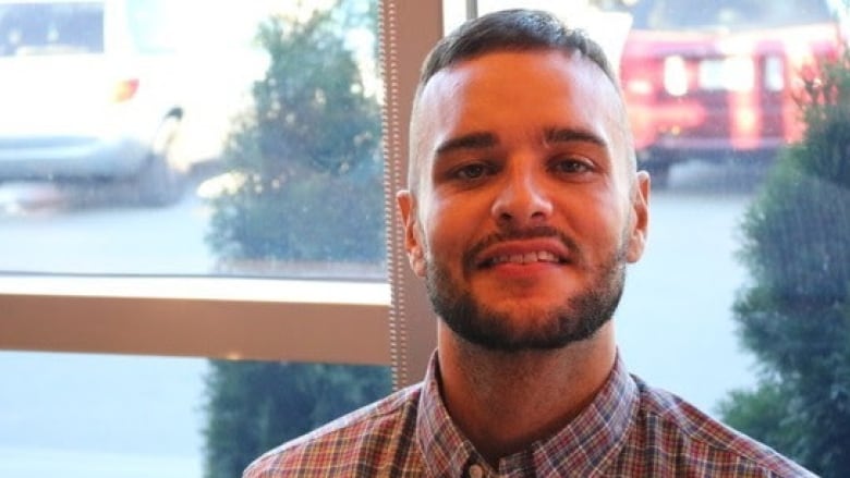 A portrait of a person in a button-up plaid shirt sitting by a window.