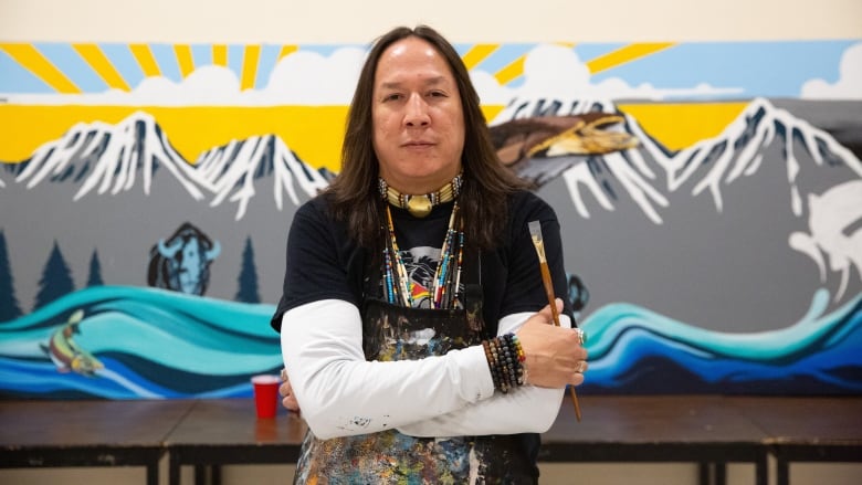 Man stands in front of a mural that shows a flowing river, mountains and a sunny sky.