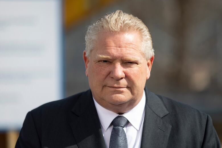 A white-haired man with a slight smile wears a suit