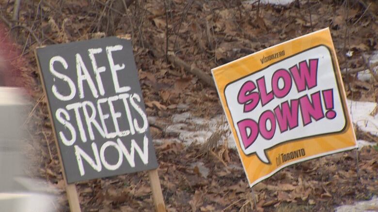 Two signs in the ground advocate for drivers to slow down, and for safer streets.