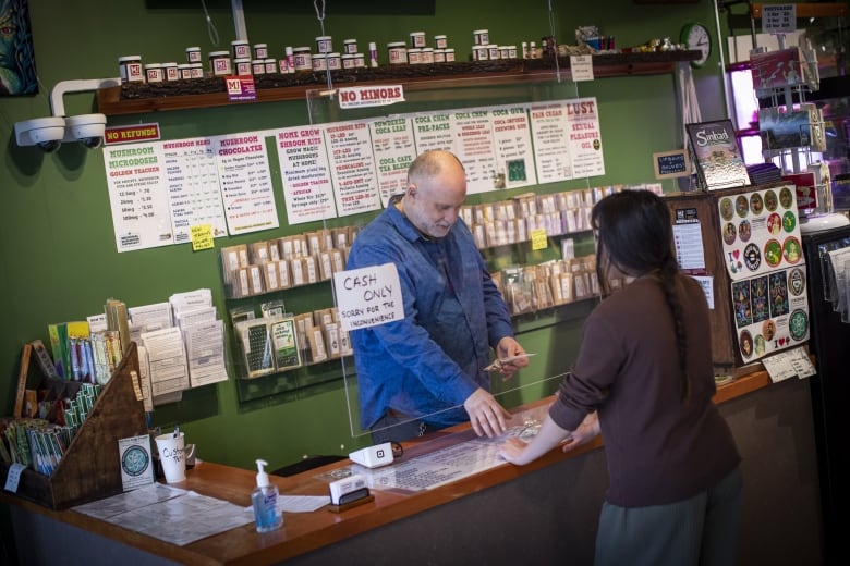 A man behind the counter involved in a transaction with a customer at a mushroom dispensary in Vancouver.