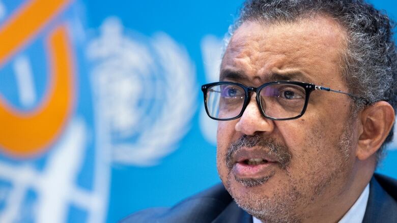 Man in glasses in front of World Health Organization background.