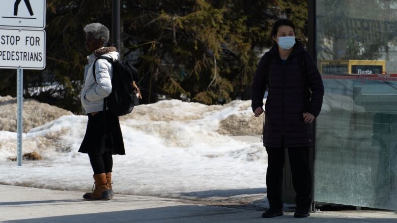 Two people wait for a public transit bus in late winter.